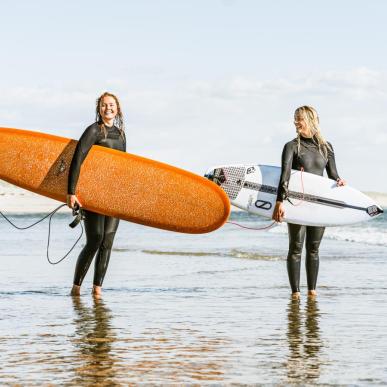 To damer som står i vandkanten med deres surfboards